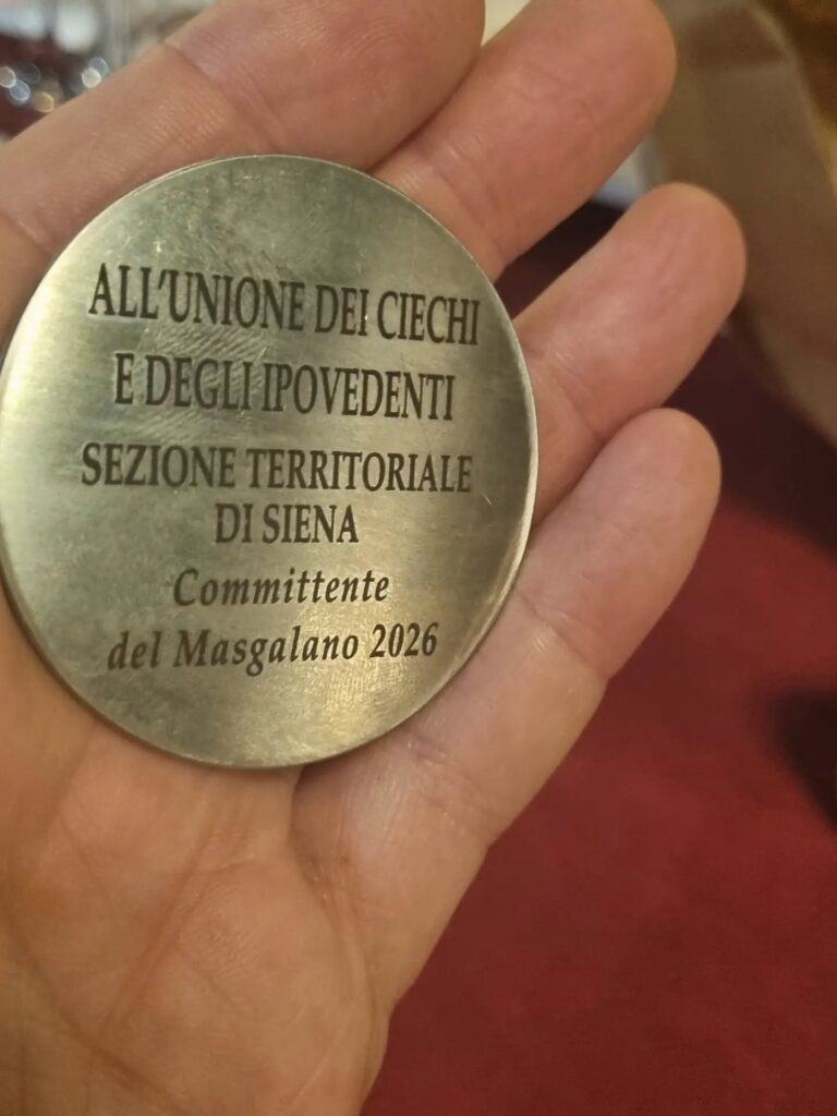 MEDAGLIA della committenza: Una medaglia circolare metallica incisa con l'iscrizione "ALL'UNIONE DEI CIECHI E DEGLI IPOVEDENTI SEZIONE TERRITORIALE DI SIENA - Committente del Masgalano 2026".