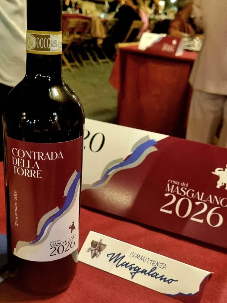 Cena del Masgalano 2026: La bottiglia di vino con etichetta personalizzata della "Contrada della Torre - 20 settembre 2026" e i segnaposto dedicati alla cena celebrativa.
